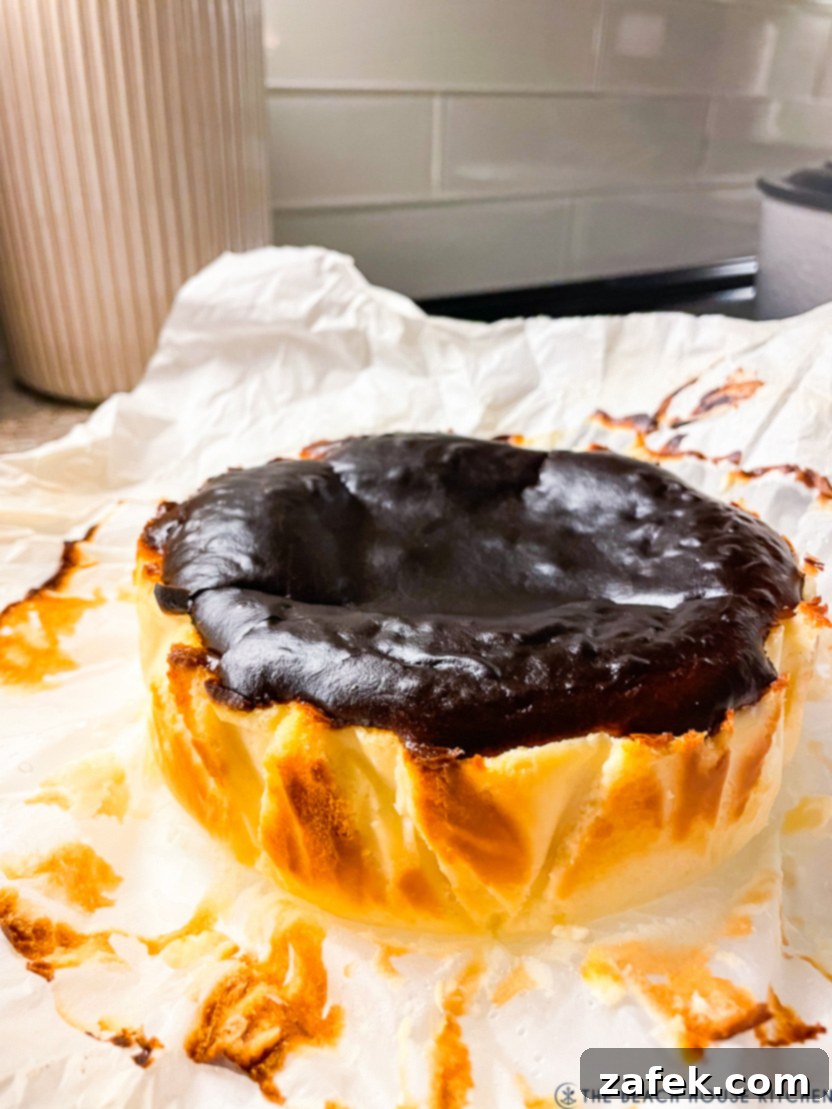 Perfect Air Fryer Basque Cheesecake 6 A top-down view of a golden-brown Air Fryer Basque cheesecake, its characteristic 'burnt' top clearly visible, nestled within a white parchment liner inside the air fryer basket.