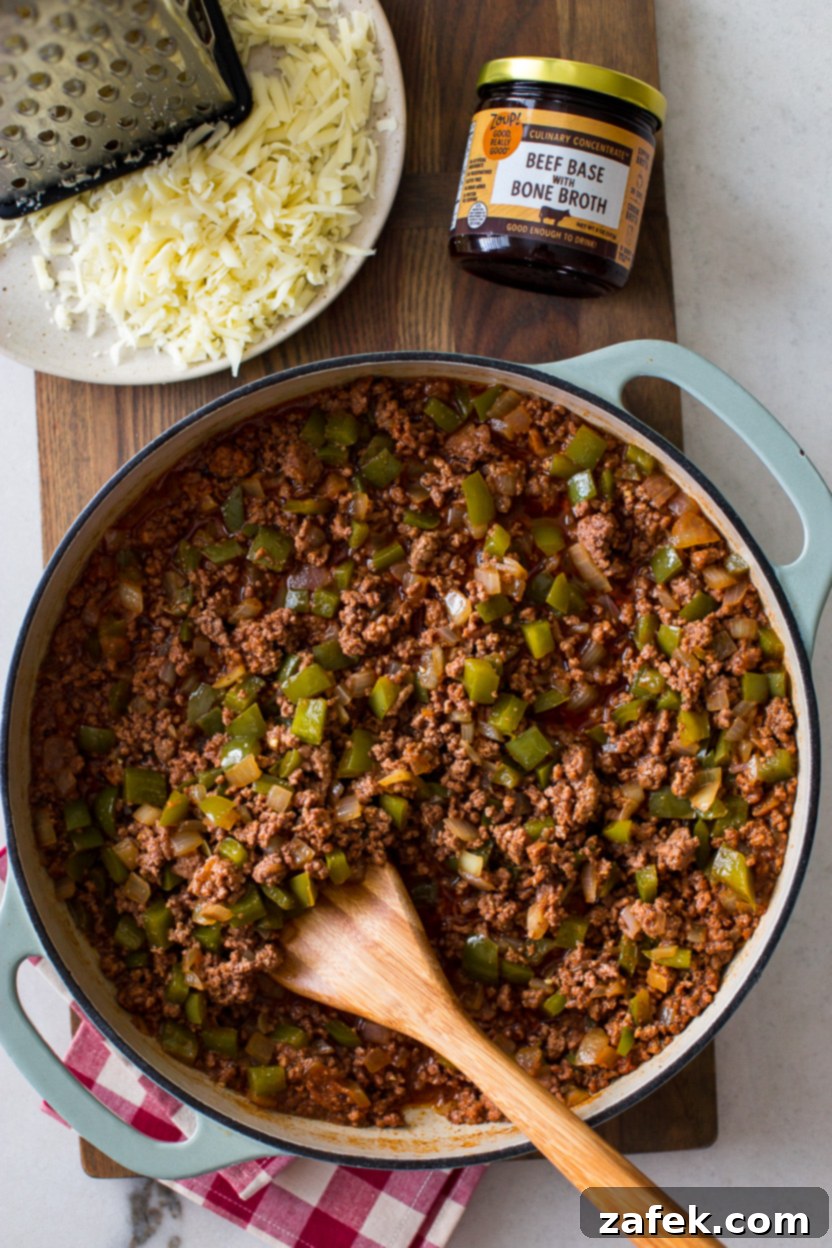 Overhead photo of a skillet overflowing with savory, cheesy Philly cheesesteak sloppy joes, garnished and ready to be served on fresh buns