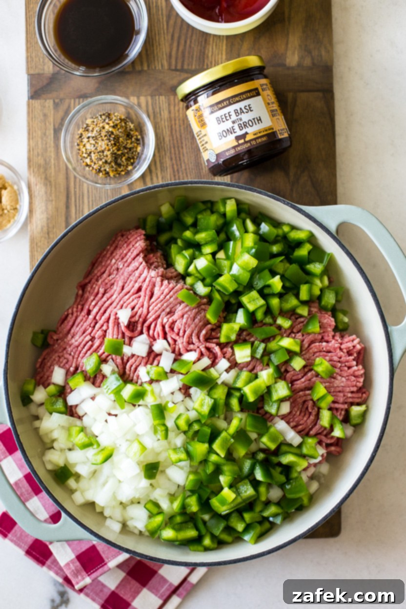 Overhead photo of a skillet containing perfectly browned ground beef, softened onions, and green peppers, showcasing the initial cooking stage before adding the sauce