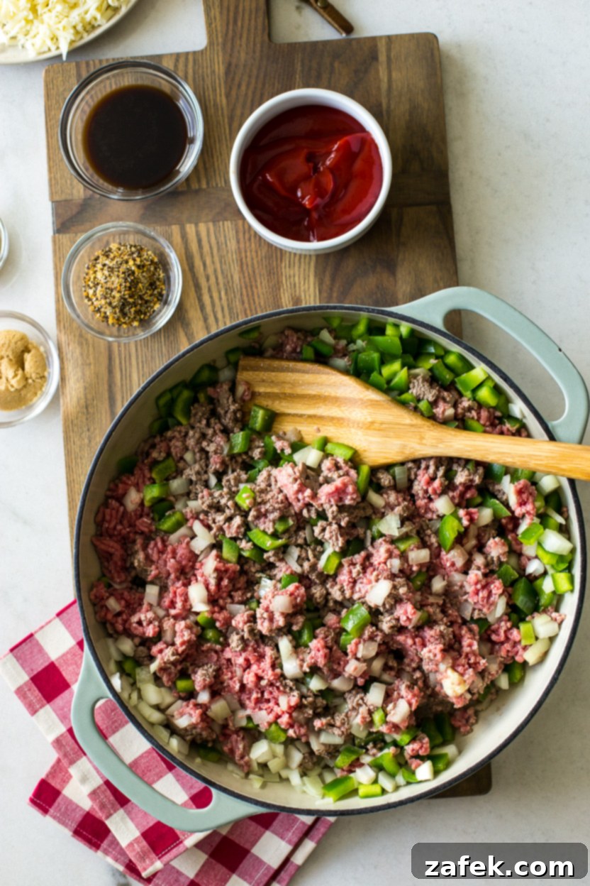 Overhead photo of a skillet with partially cooked hamburger meat, onions, and green peppers, still cooking and developing flavor