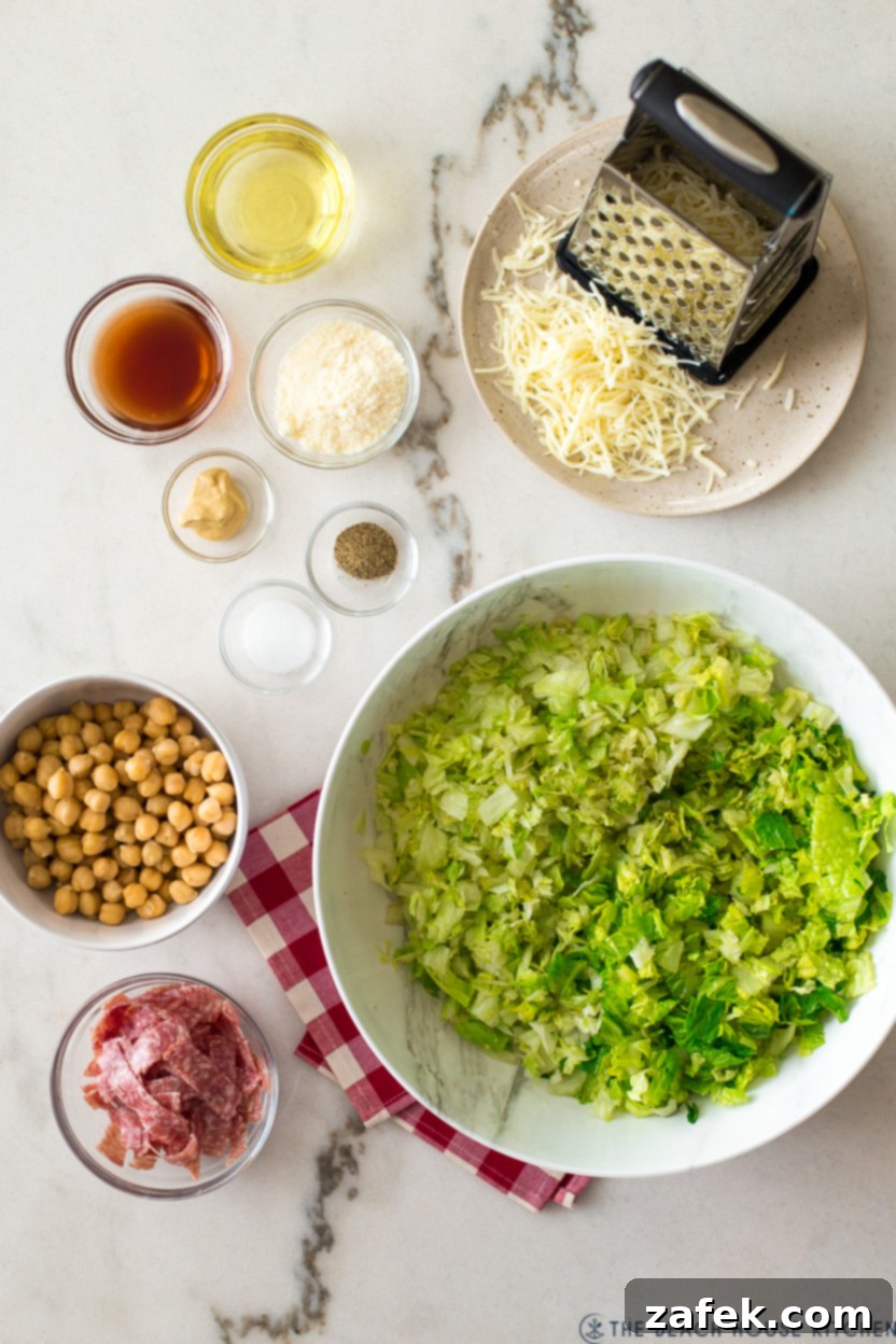 Overhead photo displaying all the fresh ingredients laid out for a chopped salad, including lettuce, salami, cheese, and chickpeas