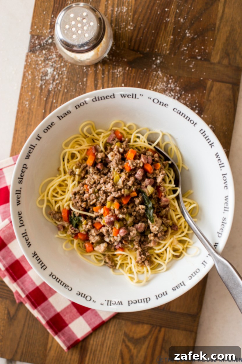 Bianco Bolognese 11 A delectable overhead photo of a bowl of perfectly cooked spaghetti generously topped with creamy White Bolognese, garnished with fresh Parmesan and a crispy sage leaf, ready to be savored.