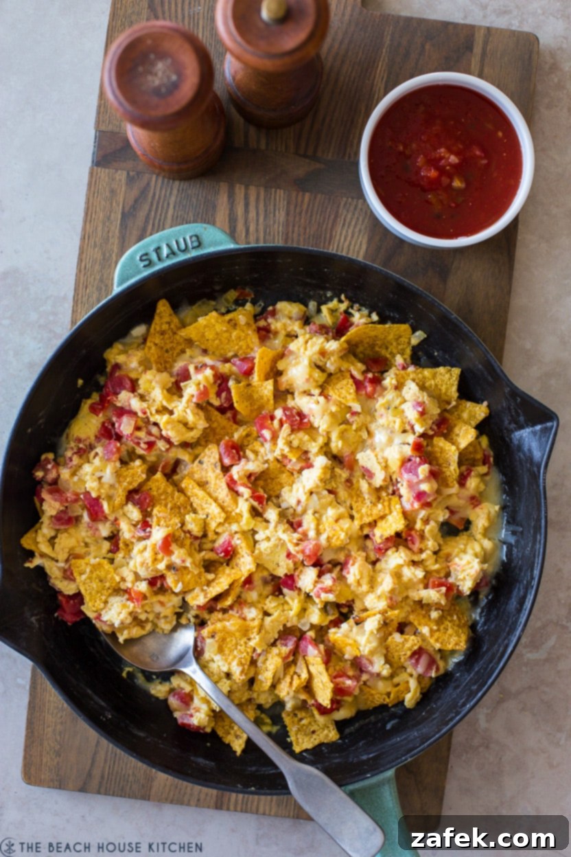 Overhead photo of a sizzling cast-iron skillet filled with freshly prepared Tex-Mex Migas, topped with a generous layer of bubbling melted cheese, ready to be served hot.