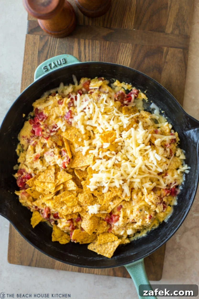A large, vibrant skillet brimming with freshly cooked Tex-Mex Migas, elegantly topped with a generous layer of perfectly melted shredded cheese and ready for serving.