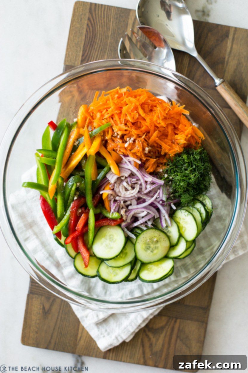 Overhead photo of a pre-tossed Easy Cucumber Salad in a glass bowl, before the dressing is fully mixed in.