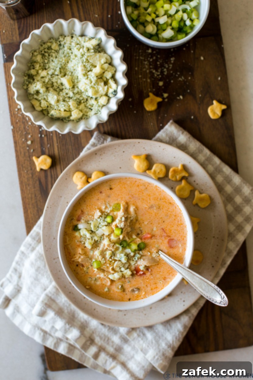 Hot Wing Soup 10 An overhead shot of a beautifully garnished bowl of Buffalo Chicken Soup, accompanied by a small bowl of fresh blue cheese crumbles.