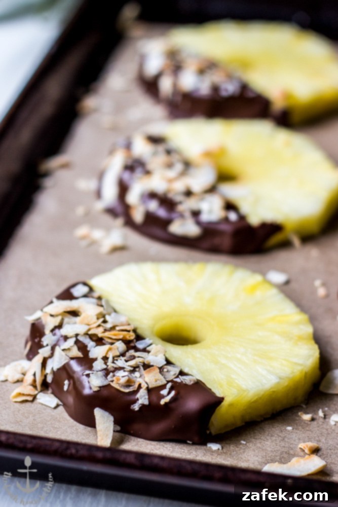 Toasted Coconut Pineapple Chocolate Treats 2 Lush chocolate-dipped pineapple slices generously sprinkled with golden toasted coconut, presented on a rustic wooden board.
