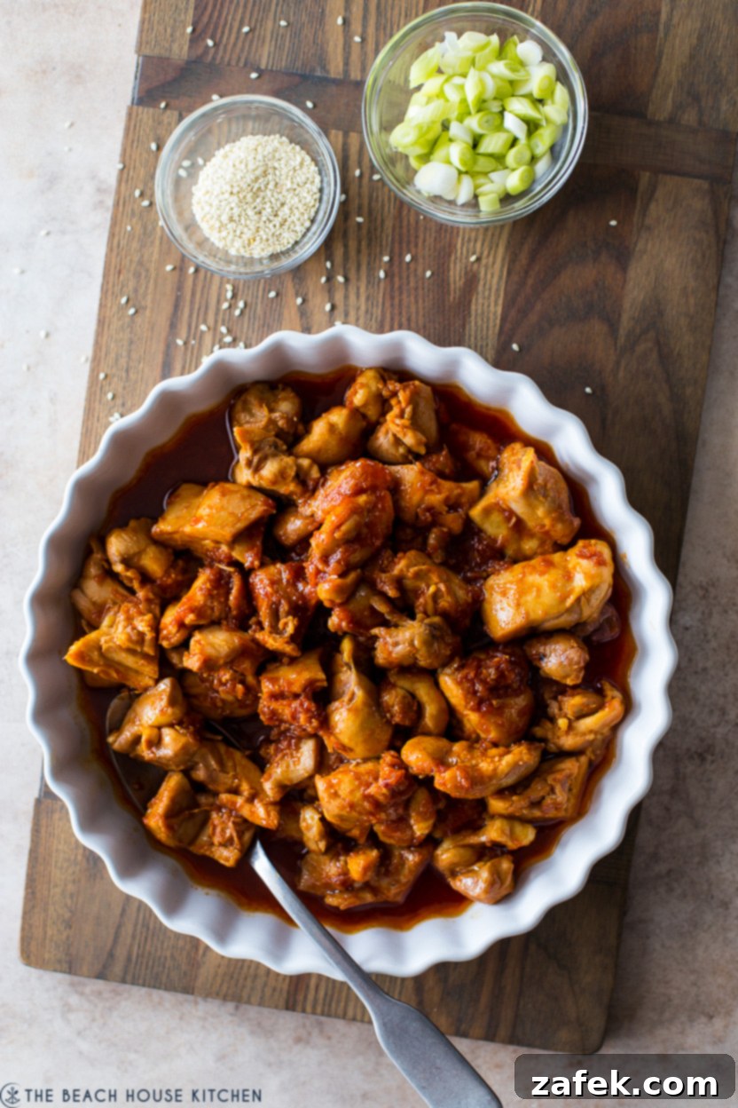 Crispy Gochujang Chicken Stir-Fry 9 Overhead photo of a round baking dish of finished gochujang chicken with a small bowl of green onions and sesame seeds for garnish.