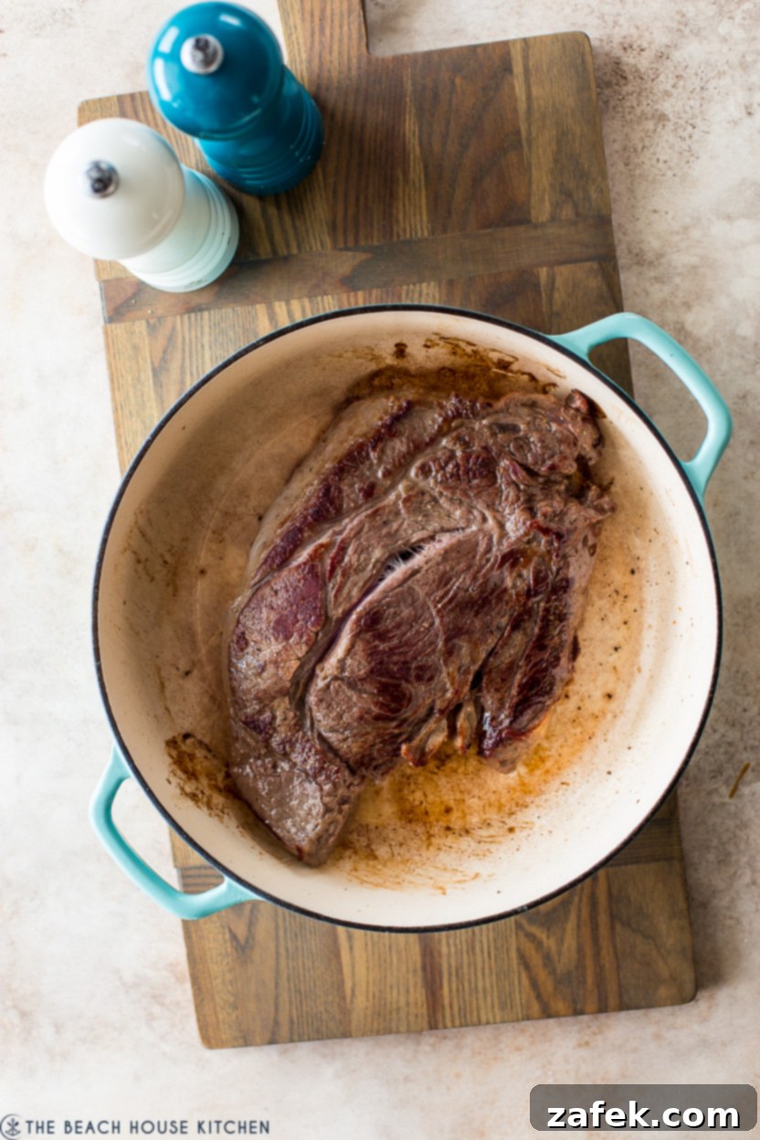 Overhead photo of a seared chuck roast in a round cat iron Dutch oven
