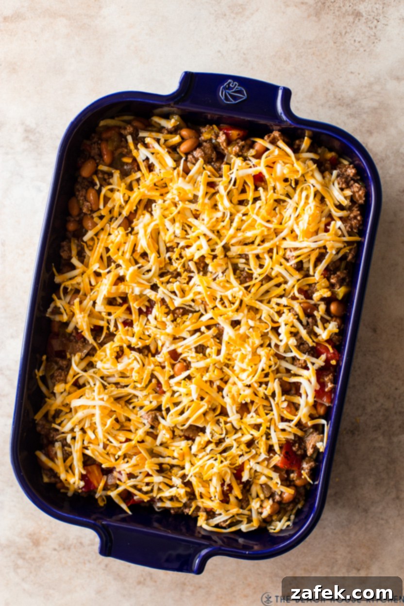 Overhead photo of a pre-baked enchilada casserole topped with shredded cheese, ready for the oven