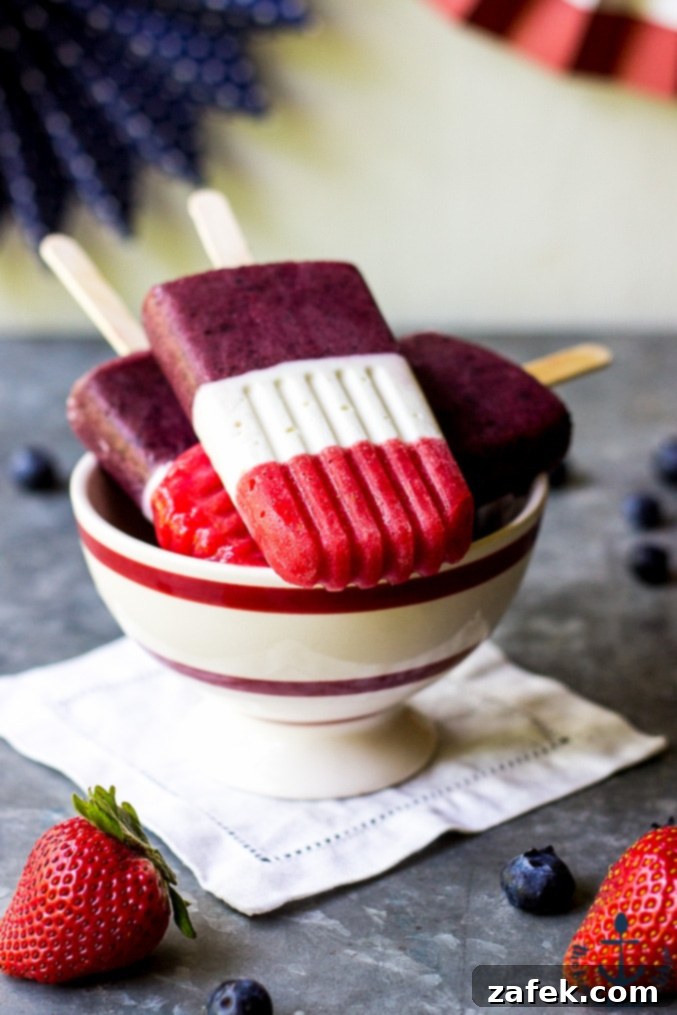 Individual Berry Cheesecake Popsicles on a rustic wooden surface.