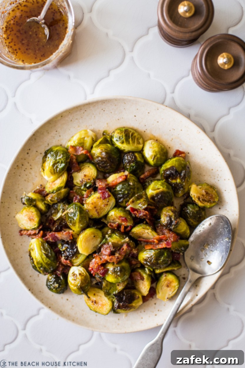 A vibrant plate of roasted Brussels sprouts topped with a glistening horseradish-honey mustard glaze and crispy bacon bits, photographed from overhead.