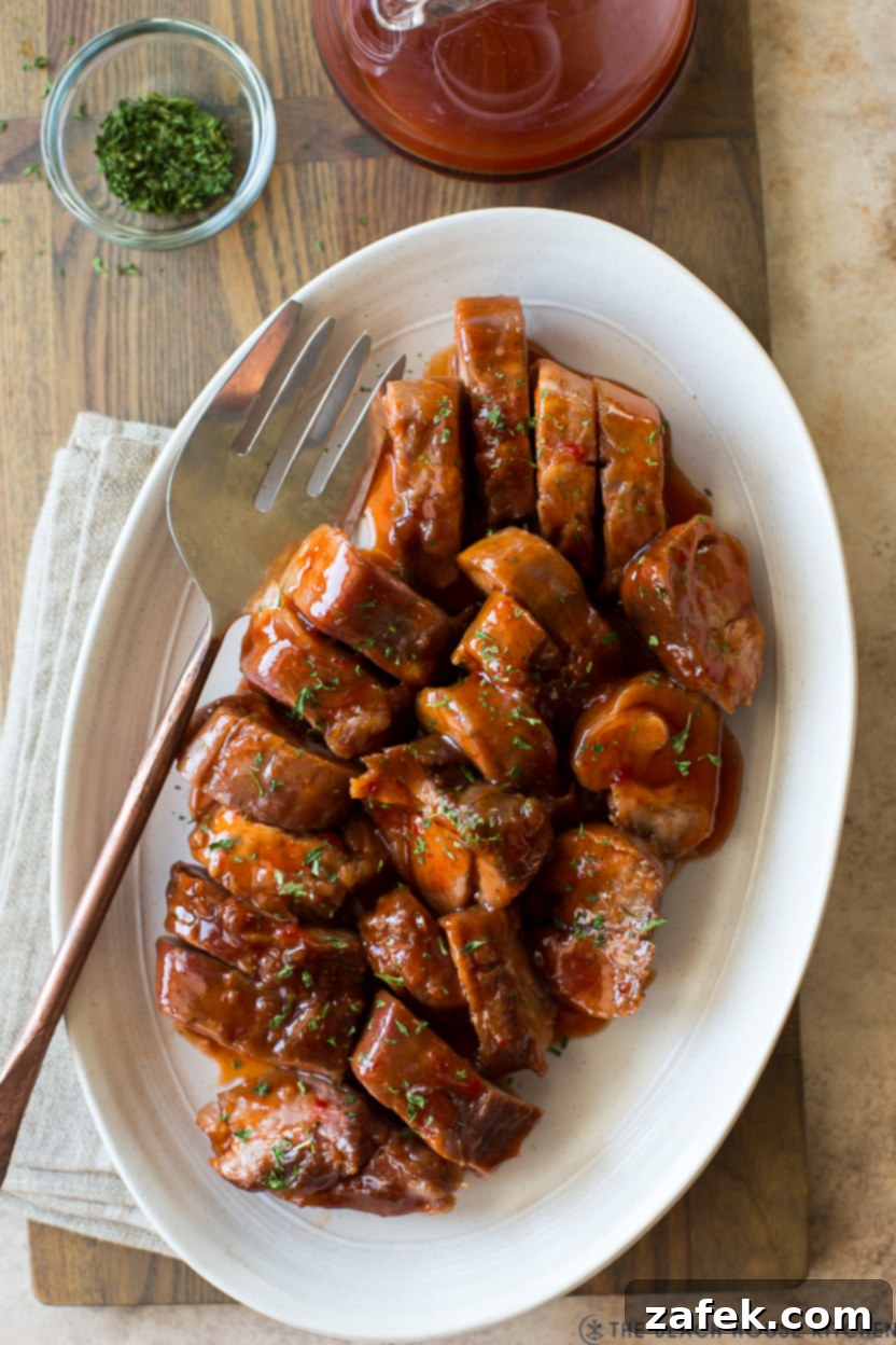 Up close overhead photo of an oval plate of pork tenderloin slices, glistening with sauce.