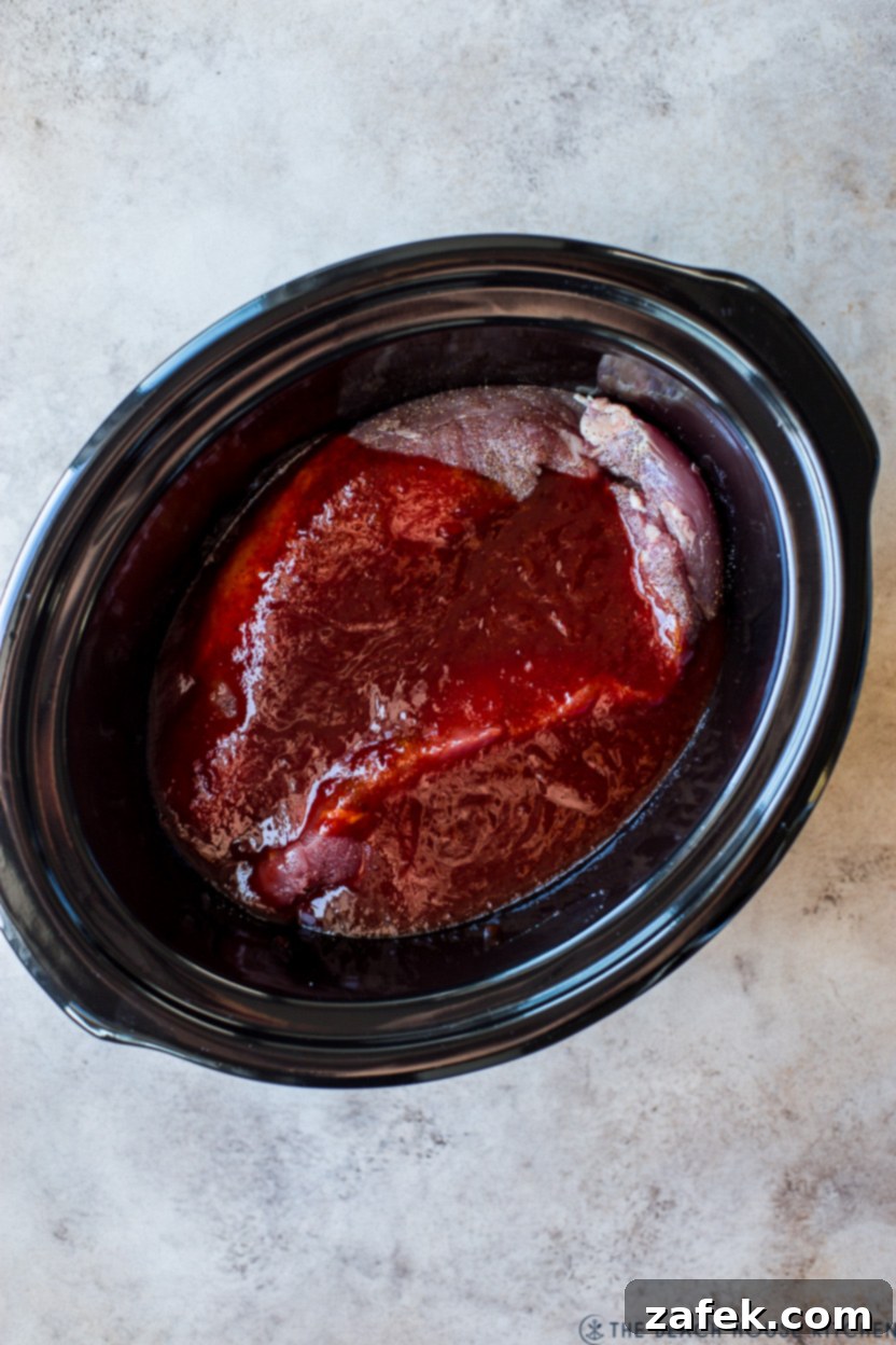 Overhead photo of pre-cooked pork tenderloins in a slow cooker, covered in sauce.