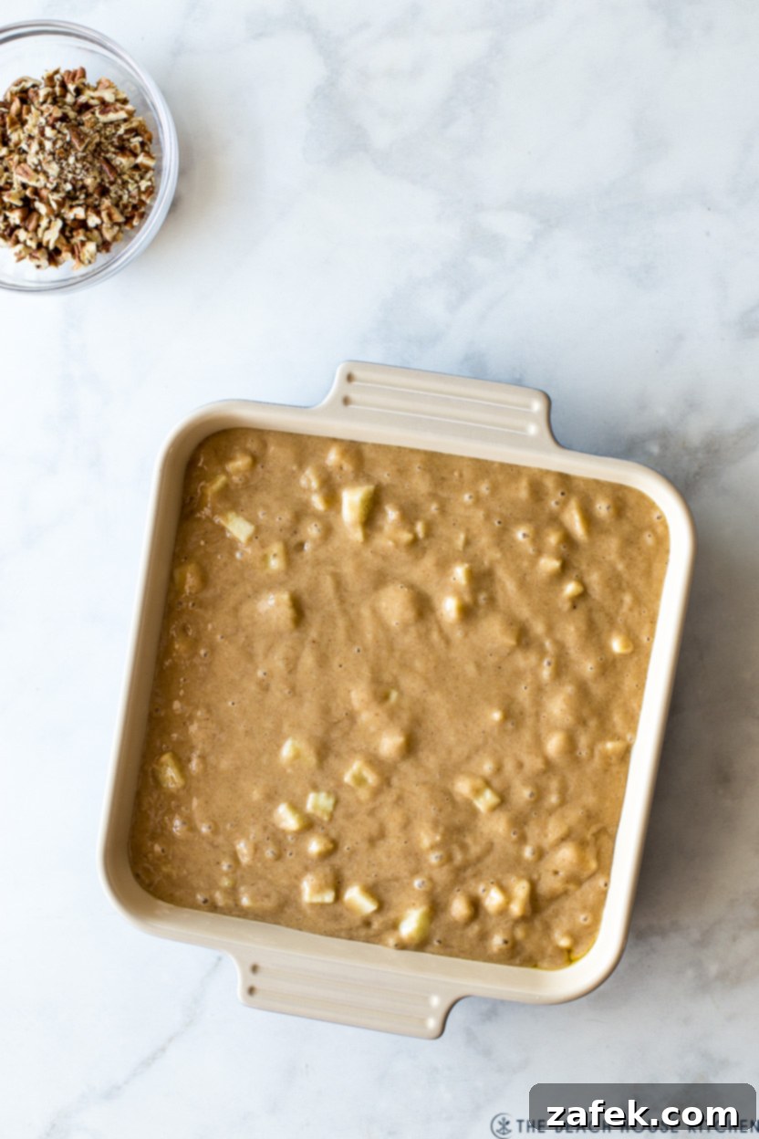 Overhead photo of a pre-baked apple snack cake batter topped with chopped pecans, ready for the oven.