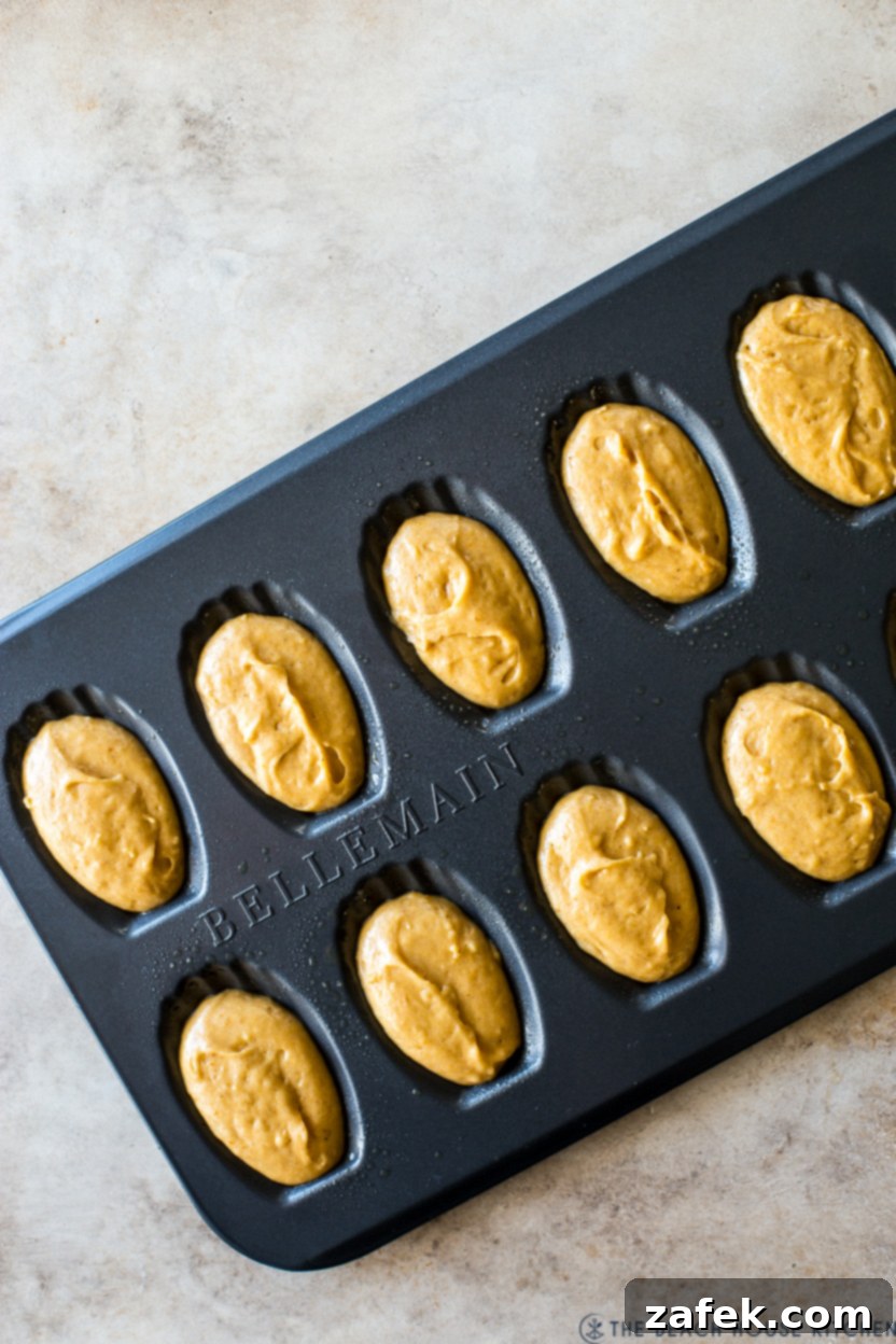 Autumn Spiced Pumpkin Madeleines 8 An overhead shot of a madeleine pan filled with unbaked pumpkin madeleine batter, ready to be placed in the oven, showcasing the precise filling of each shell.