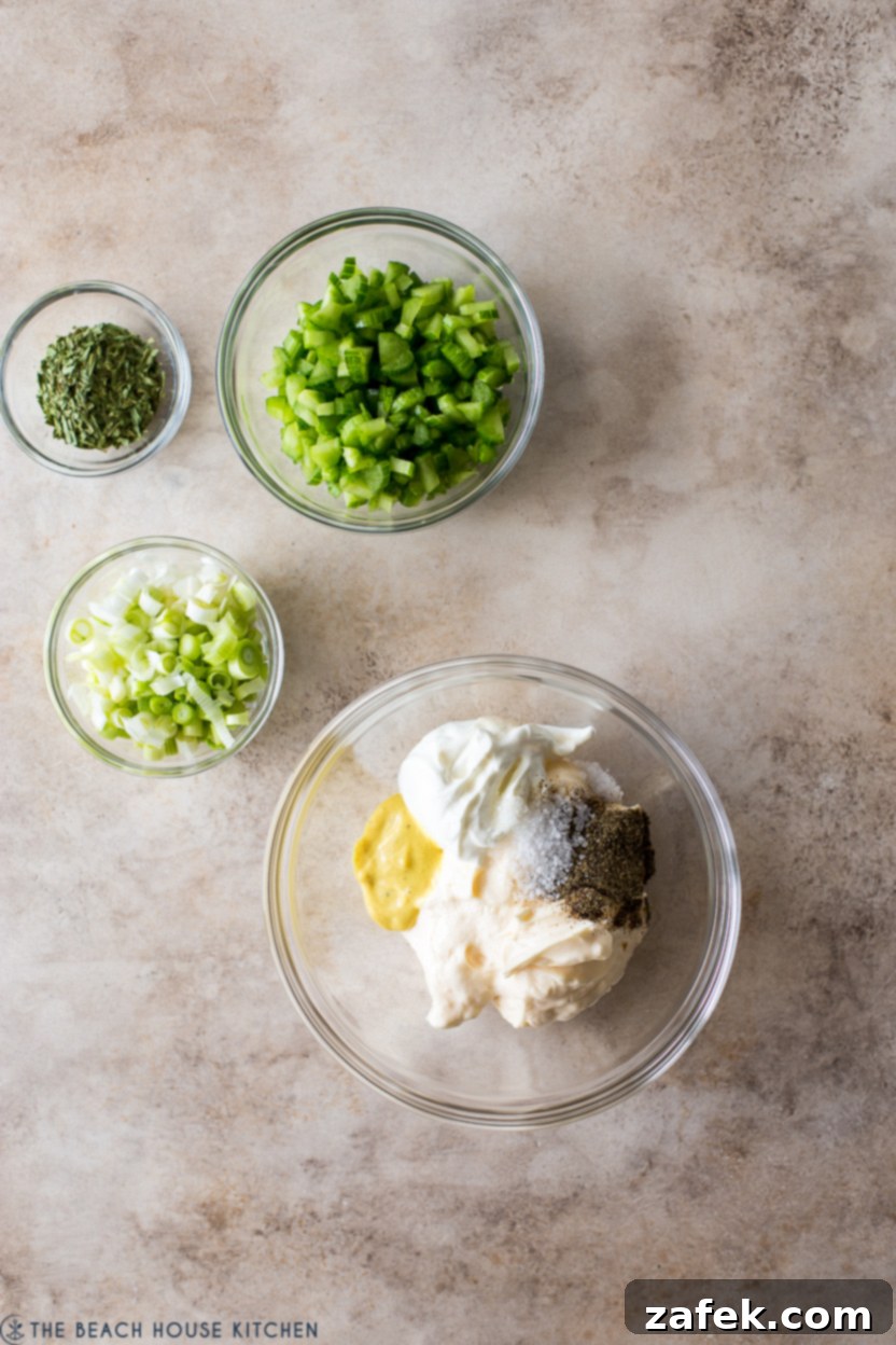Overhead photo of a small bowl of finely chopped celery, sliced scallions, and dried tarragon next to a bowl of dressing ingredients.