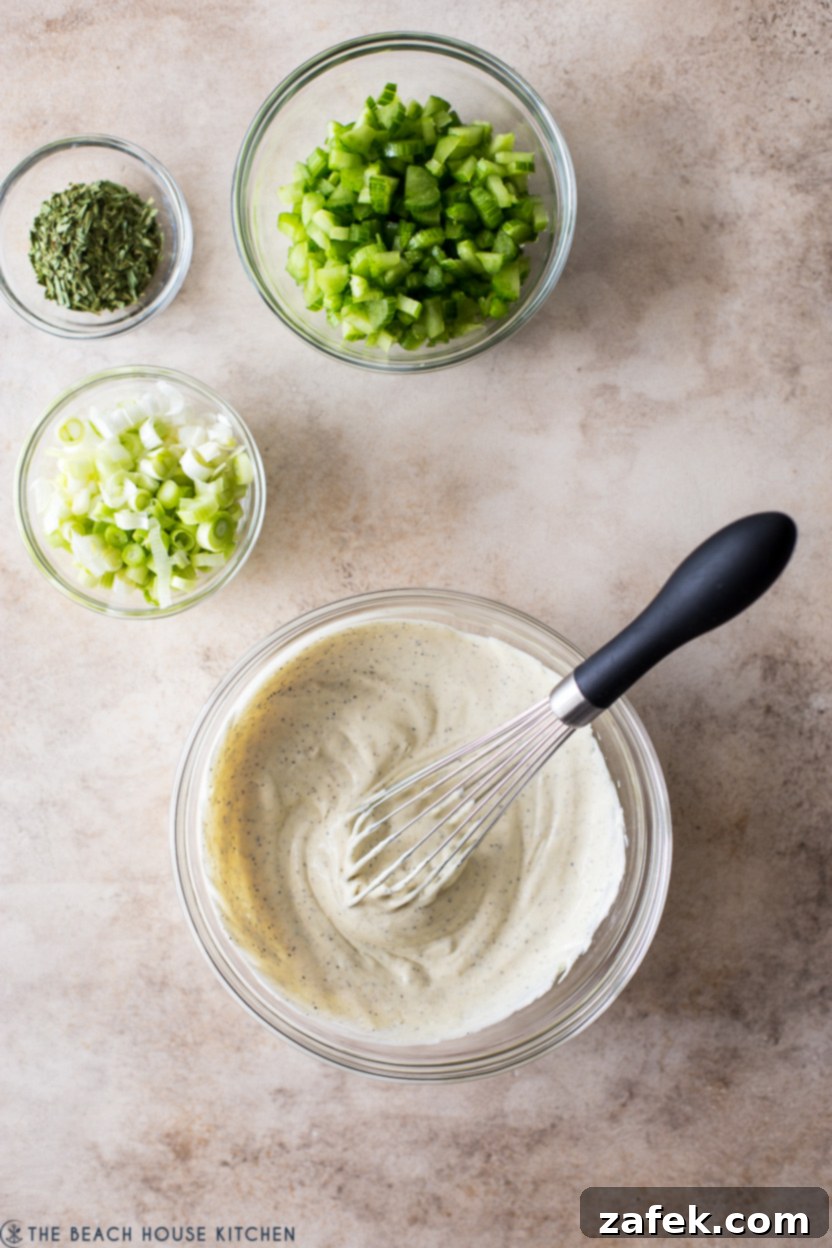 Overhead photo of the creamy dressing mixture for chicken salad alongside a bowl of chopped celery, scallions, and dried tarragon.