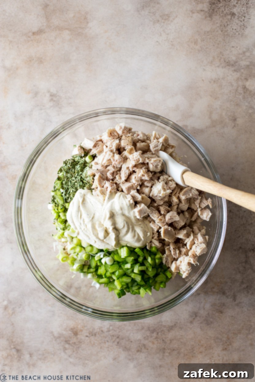 Overhead photo of a bowl of chicken salad ingredients, with a generous dollop of creamy dressing on top, ready to be mixed.