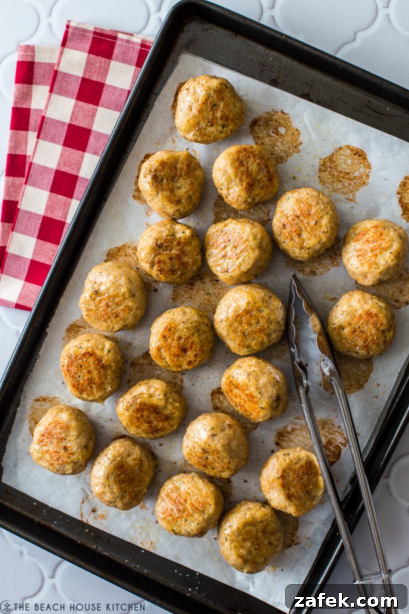 A baking sheet filled with golden brown, perfectly baked chicken meatballs, ready to be served or stored.