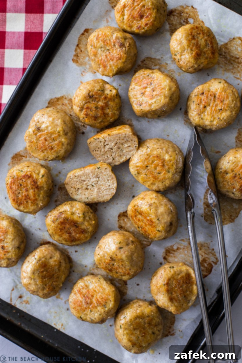 A close-up, overhead view of succulent chicken meatballs arranged on a parchment-lined baking sheet, showcasing their golden-brown exterior and inviting texture.
