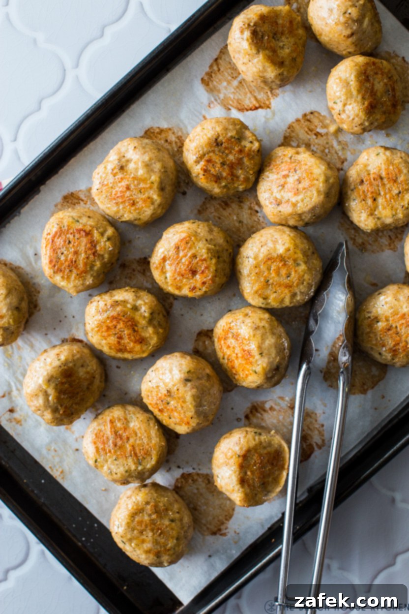 A close-up view of freshly baked, golden-brown chicken meatballs, perfectly cooked and ready to be enjoyed, on a baking sheet.