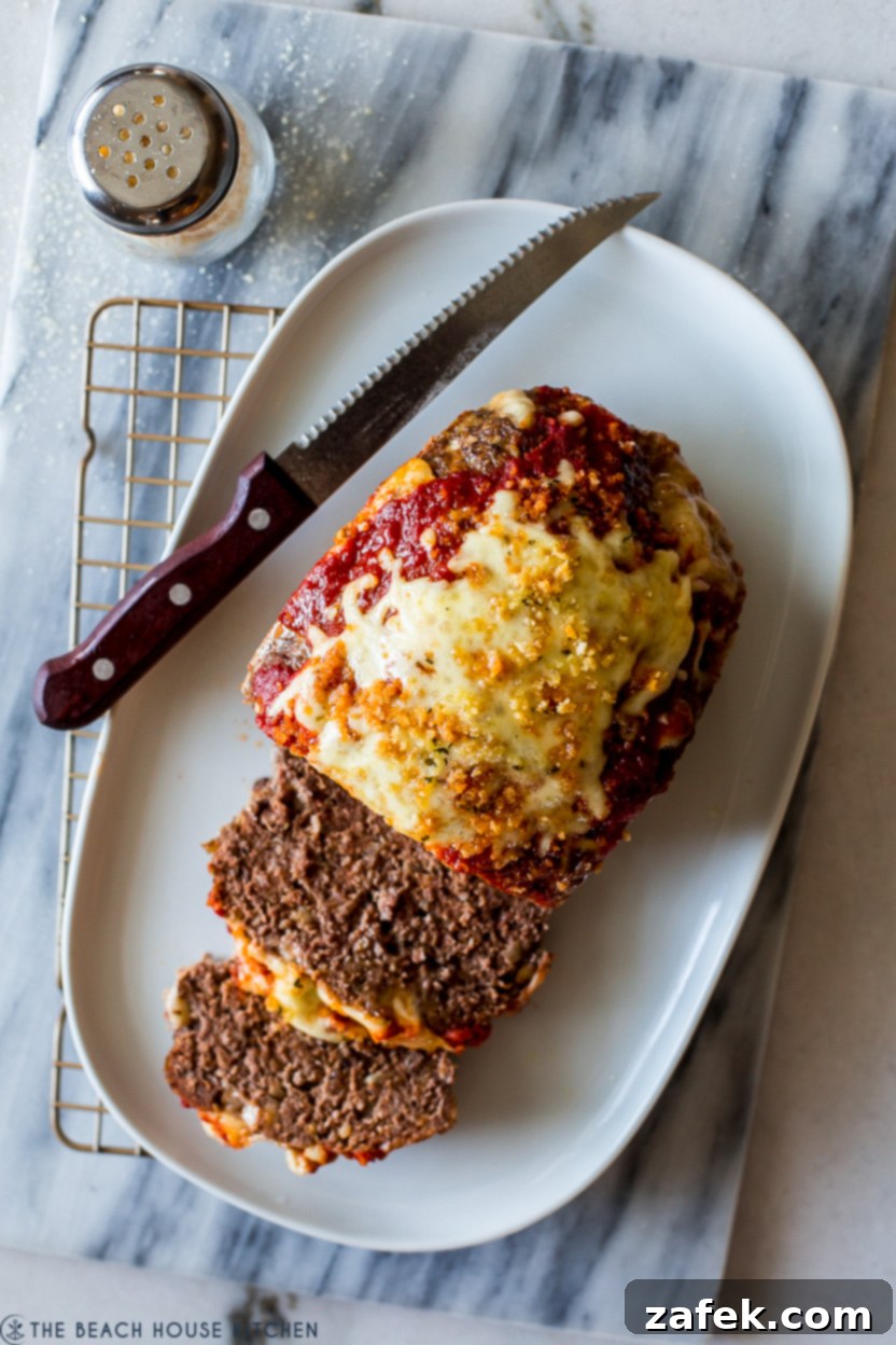Overhead photo of an oval platter with a perfectly sliced Italian Meatloaf and a sharp serrated knife, ready to serve.