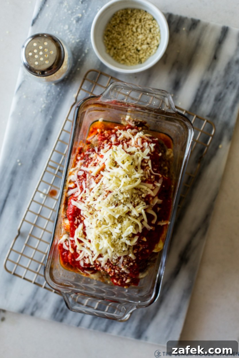 Overhead photo of a pre-baked meatloaf in a pan, now topped with marinara sauce, shredded cheese, and panko, ready for final baking.