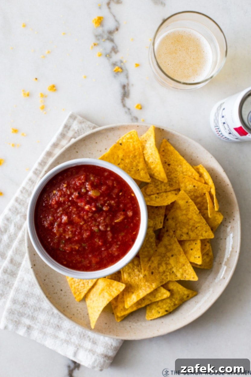 Overhead photo of a bowl of salsa on a plate with tortilla chips with a glass of beer off to the side