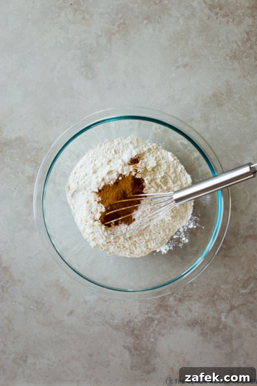 Sweet Maple Blueberry Pancake Muffins 5 Overhead photo of a clear glass bowl containing a perfectly combined mixture of flour and cinnamon, with a whisk resting in it