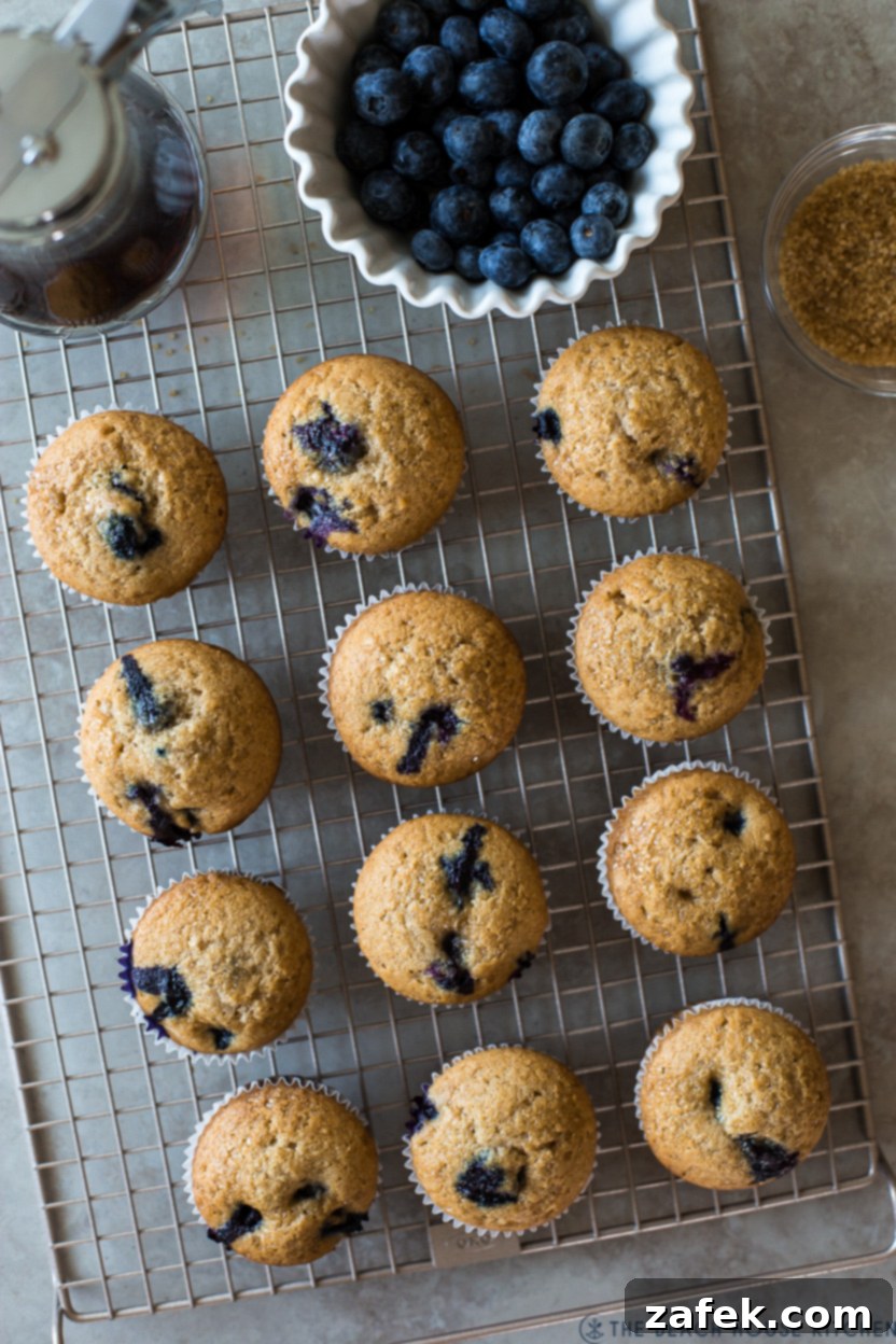 Sweet Maple Blueberry Pancake Muffins 10 Overhead photo of golden-brown Maple Blueberry Pancake Muffins cooling on a wire rack, with a small bowl of fresh blueberries for garnish