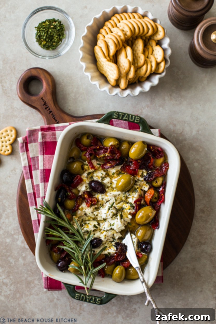 Overhead photo of Baked Feta with Olives and Sun-dried Tomatoes, garnished with fresh herbs, ready to be served with crusty bread.
