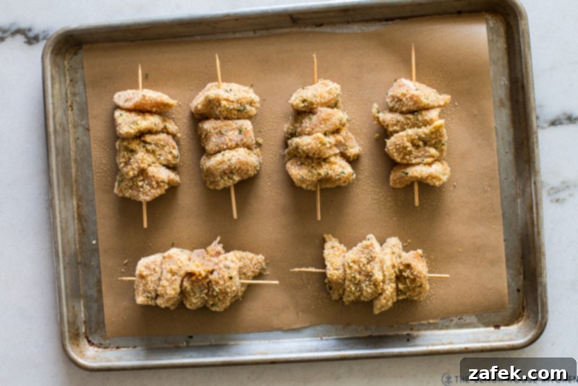 Overhead photo of a baking sheet of pre-baked chicken on skewers