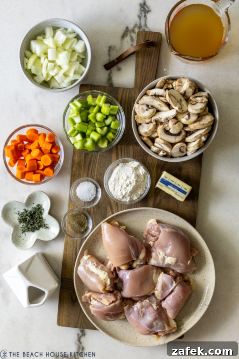 Overhead photo of fresh ingredients laid out for chicken fricassee, including chicken thighs, mushrooms, onions, carrots, celery, and herbs.