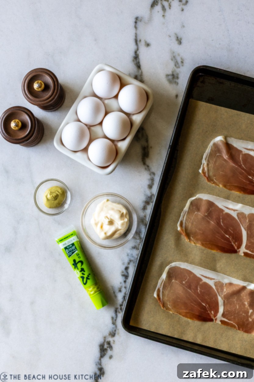 Overhead photo of the key ingredients for wasabi deviled eggs laid out: eggs, mayonnaise, Dijon mustard, wasabi paste, and prosciutto slices