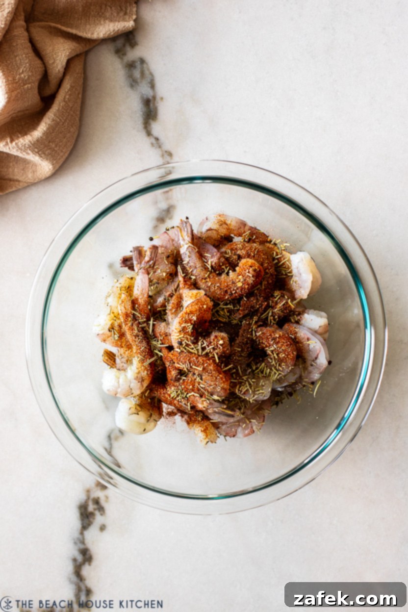 Overhead photo of a glass bowl filled with raw shrimp topped with a spice mixture