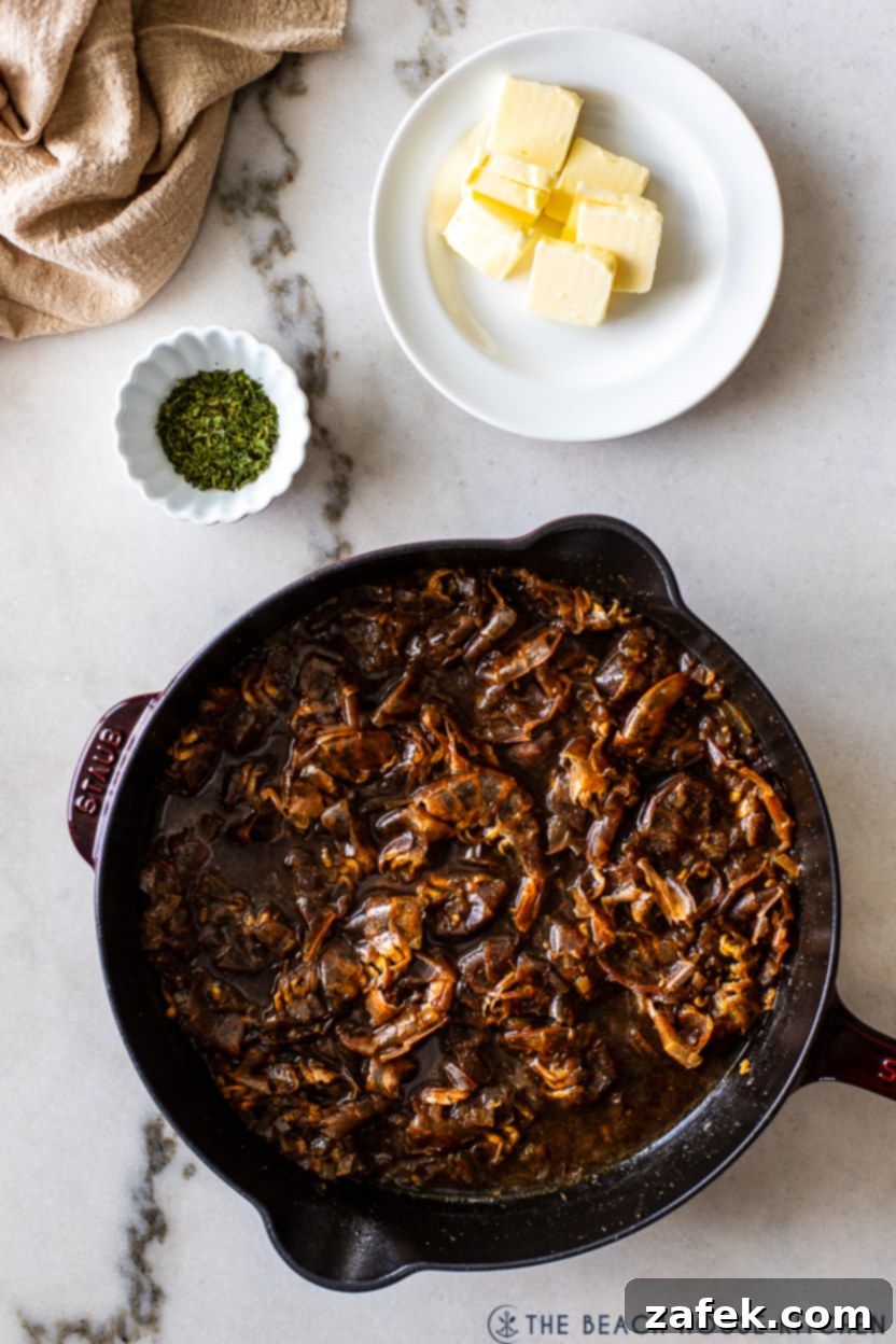 Overhead photo of a skillet filled with shrimp shells and a bbq base with a plate of butter patties and a small bowl of chopped parsley