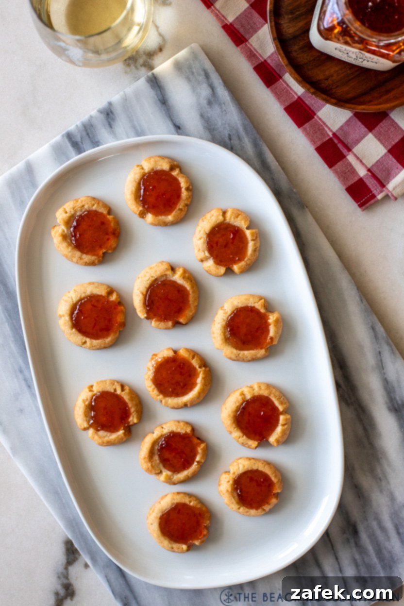 Overhead photo of an oval white plate of cheesy thumbprints with red pepper jelly, ready to serve at a party.