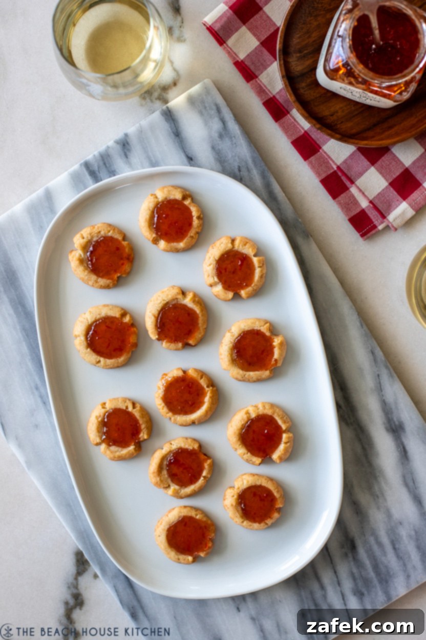 Overhead photo of a white plate beautifully arranged with cheesy thumbprints featuring red pepper jelly, showcasing their golden-brown edges.