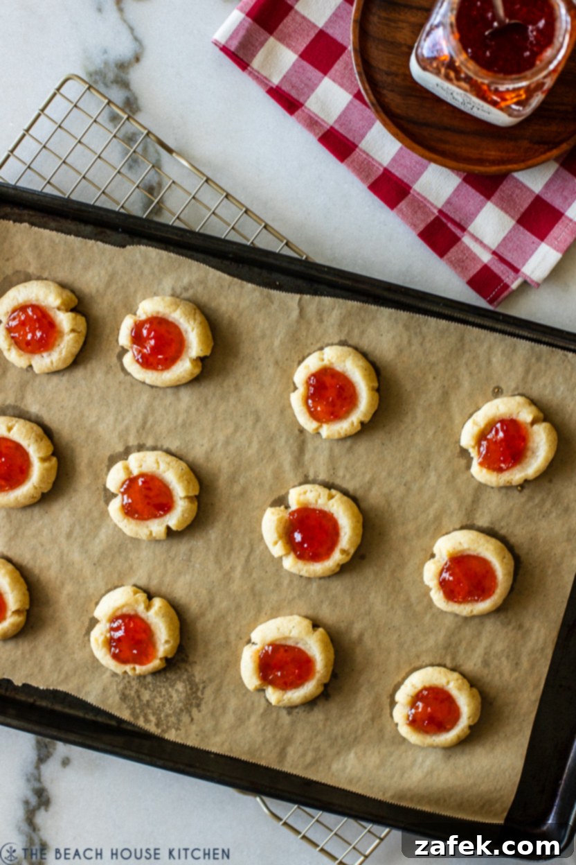 Overhead photo of baked thumbprints with their indents filled with glistening red pepper jelly, ready for the final bake.