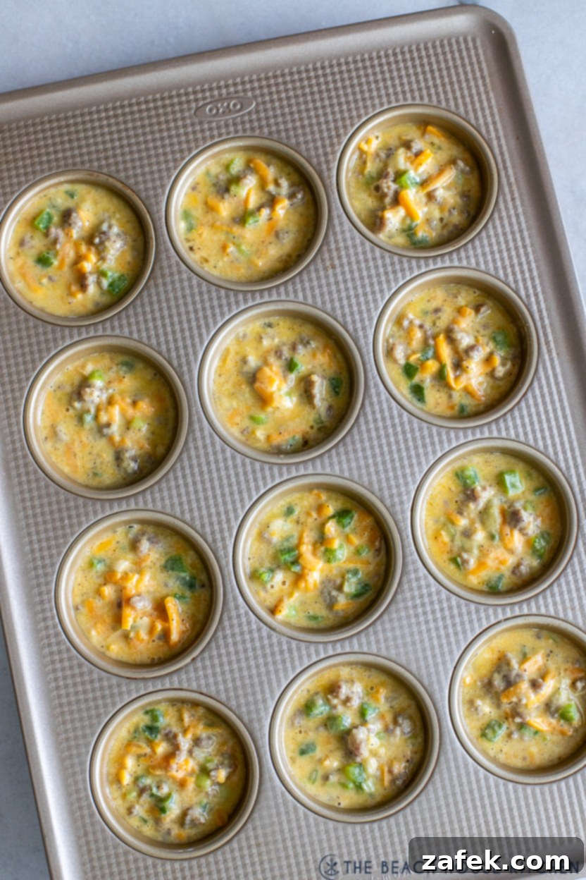 Overhead photo of unbaked egg breakfast muffin mixture scooped into a muffin tin, ready for the oven.