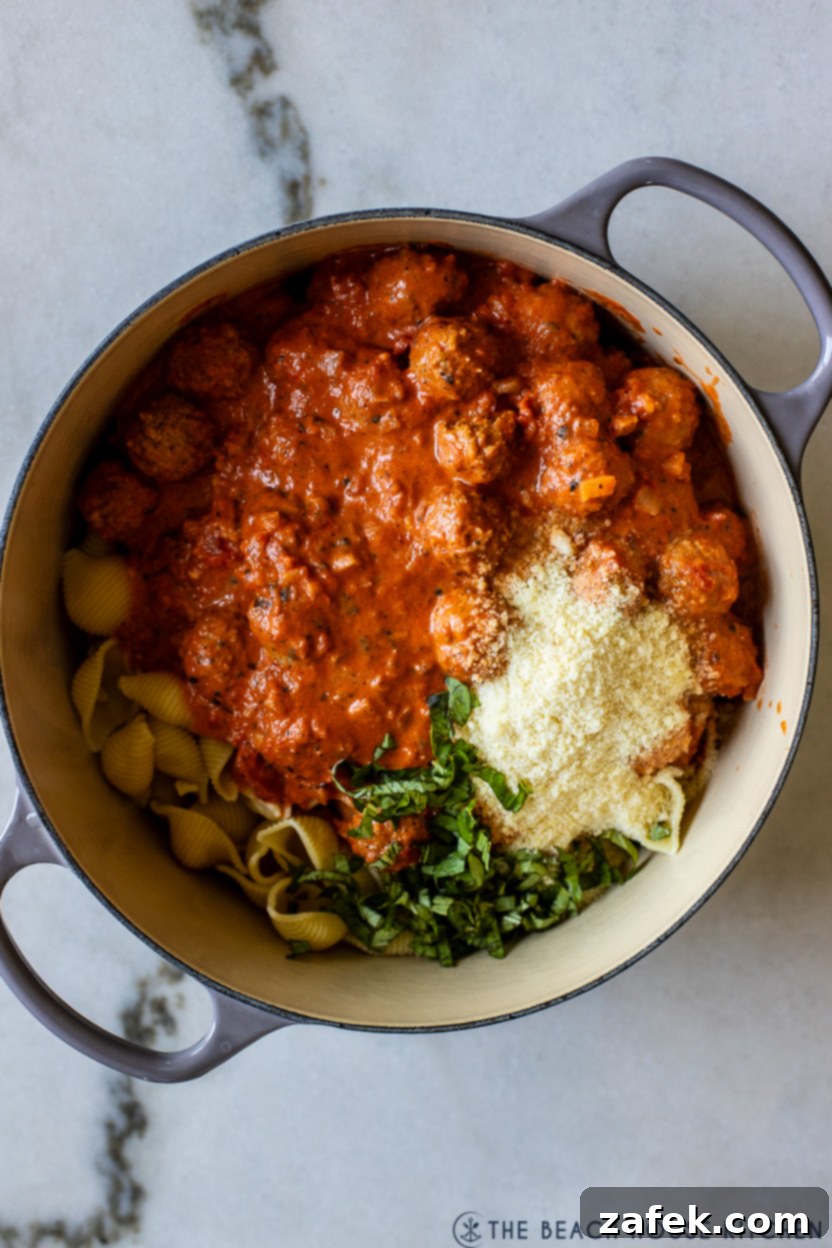 Heavy cream being stirred into the simmering meatball and tomato sauce