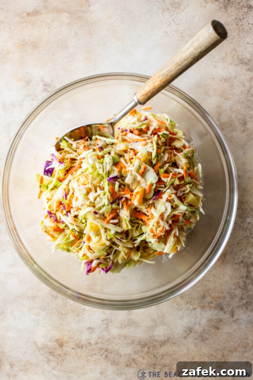 Overhead photo of a glass bowl of pineapple coleslaw with a spoon in it, showcasing its refreshing texture and vibrant colors