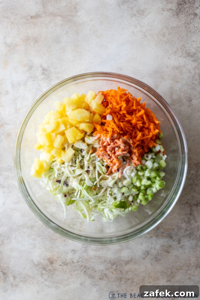 Overhead photo of a glass bowl with pre-mixed pineapple coleslaw ingredients before dressing is added