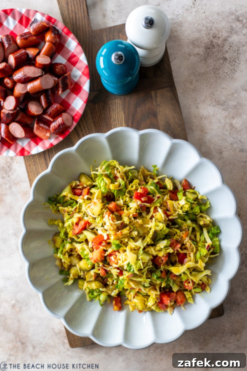 Close-up overhead photo of a beautifully presented Chicago Hot Dog Salad, mounded high on a white serving plate and generously topped with perfectly sliced, seared hot dogs, ready to be enjoyed as a refreshing meal.