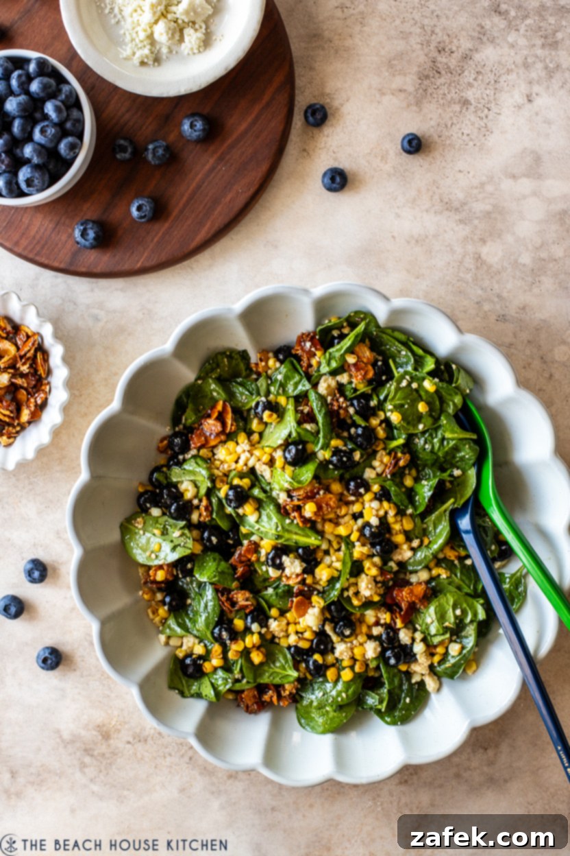 Overhead photo of a white scalloped platter filled with a vibrant blueberry corn salad, garnished with fresh mint leaves.