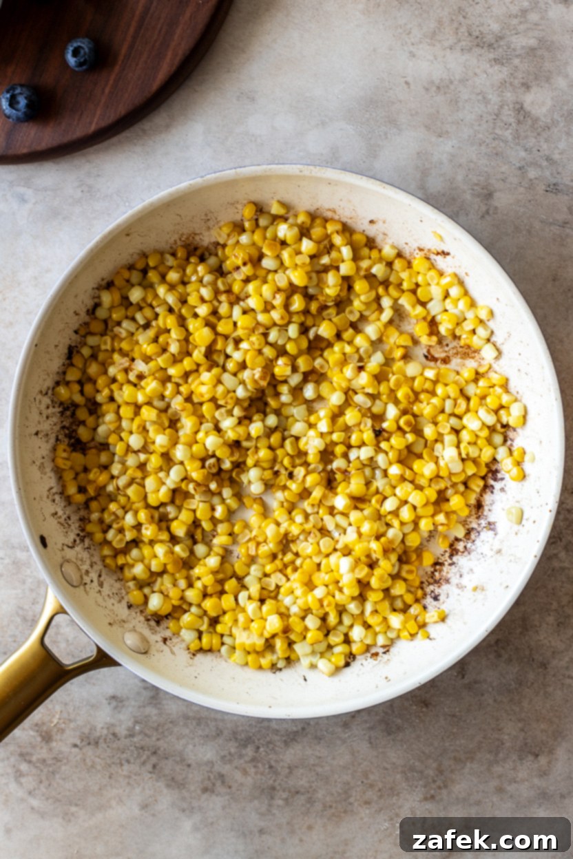 Overhead photo of a cast iron skillet filled with lightly browned, sautéed corn kernels, signifying a key preparation step for the salad.