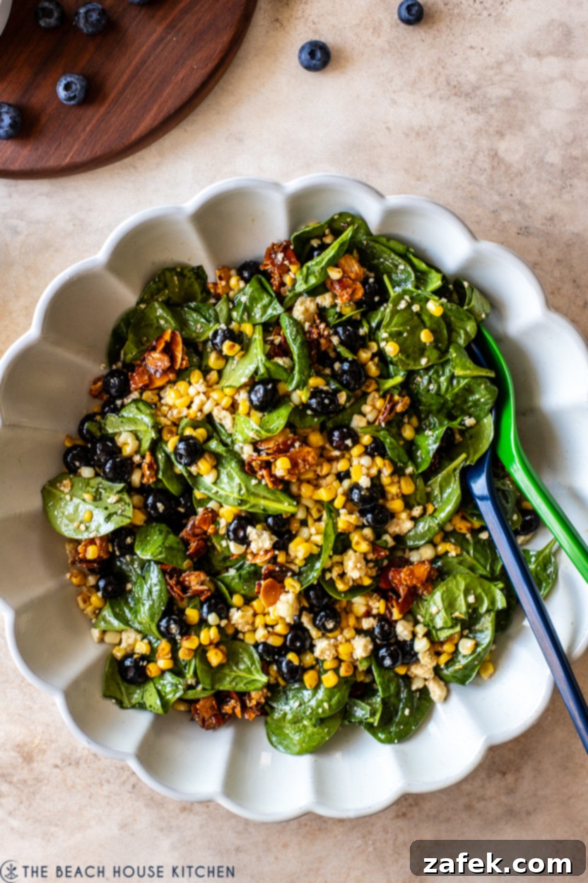 Up close overhead photo of a vibrant Blueberry Corn Salad in a white bowl, showing the textures of blueberries, corn, spinach, and almonds.