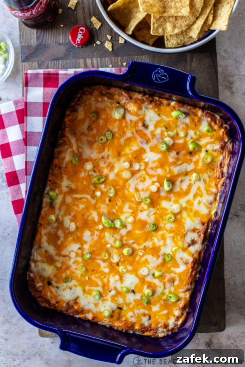 Creamy, cheesy, and spicy Texas Trash Dip in a vibrant blue baking dish, garnished with fresh green scallions, ready to be served hot.
