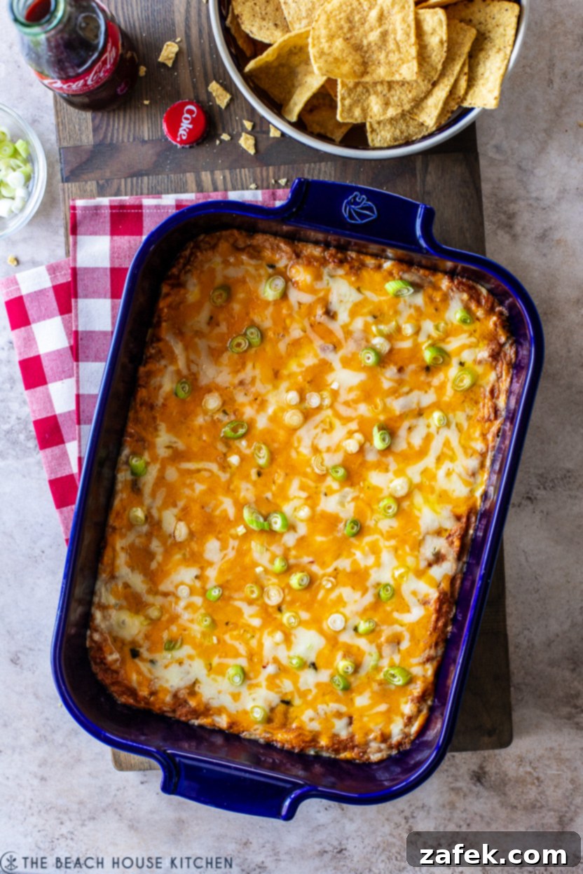 Golden brown and bubbly Texas Trash Dip in a blue ceramic baking dish, fresh out of the oven and garnished with vibrant green scallions, ready for serving.